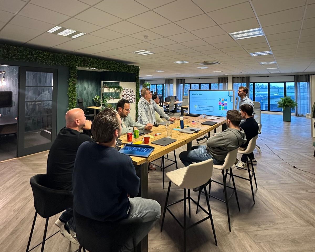 Een groep professionals tijdens een interactieve AI-workshop aan een houten tafel in een modern kantoor, kijkend naar een presentatiescherm met de tekst 'Wat is AI?'