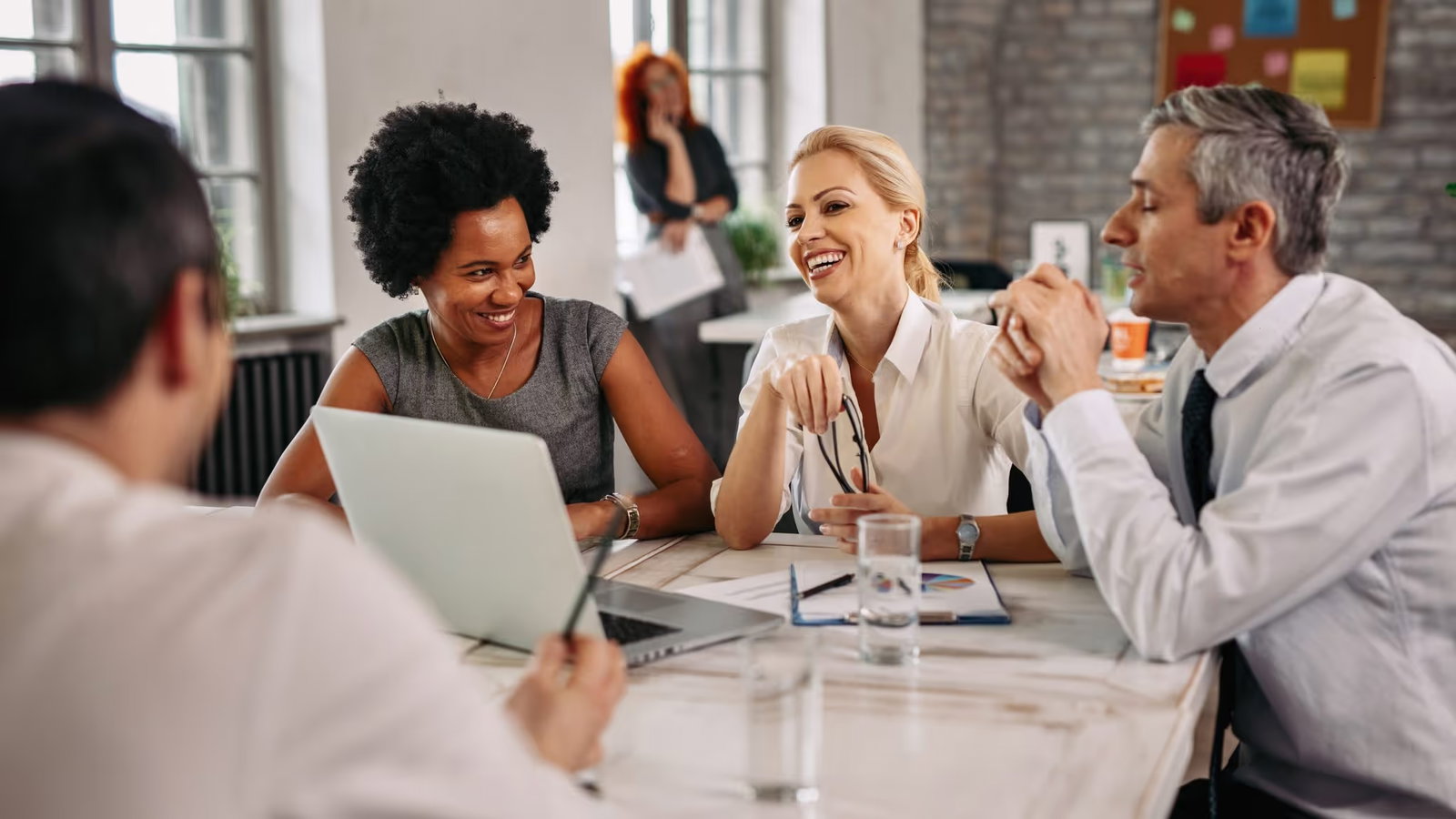 Een diverse groep van vier professionals die enthousiast overleggen rondom een laptop in een modern, licht kantoor.