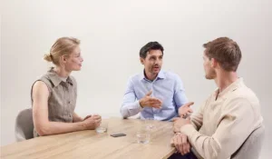 Drie professionals in gesprek, waarbij een AI-voice recorder op tafel de vergadering notuleert.