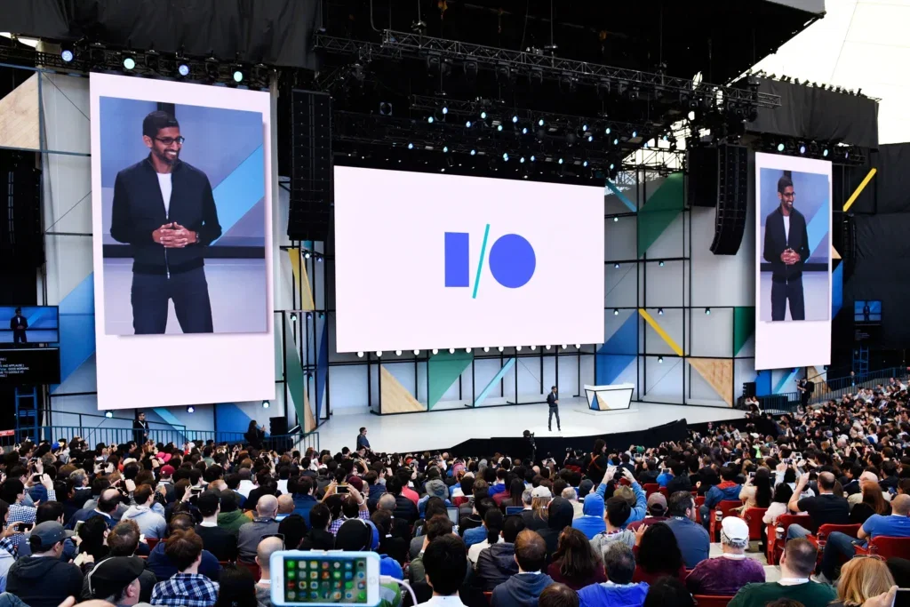 Sundar Pichai presenteert op het grote podium tijdens de Google I/O conferentie voor een volle zaal met ontwikkelaars en tech-enthousiastelingen.
