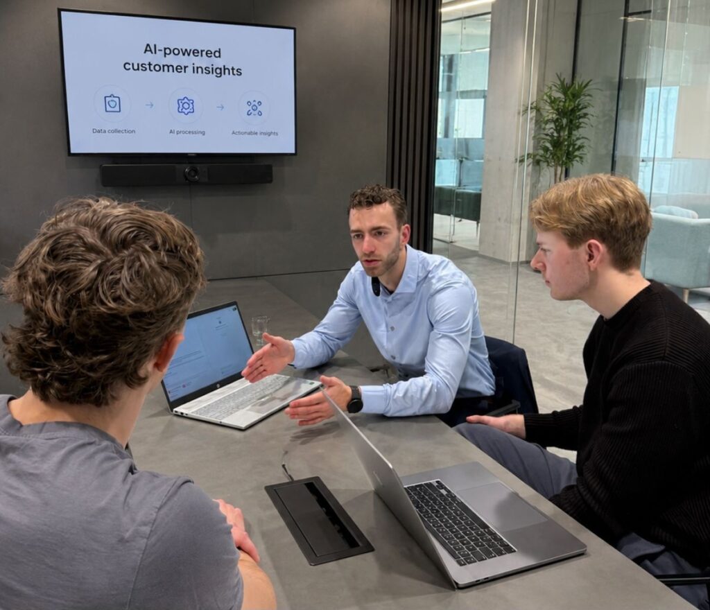 Lumans aan een vergadertafel met laptops, die een presentatiescherm met de stappen 'Data collection', 'AI processing' en 'Actionable insights' bespreken met een klant.